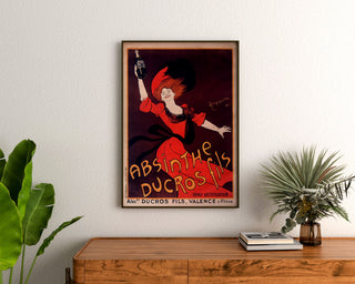 Manifesto pubblicitario vintage Absinthe Ducros, incorniciato sopra una cassettiera in legno, tra piante.