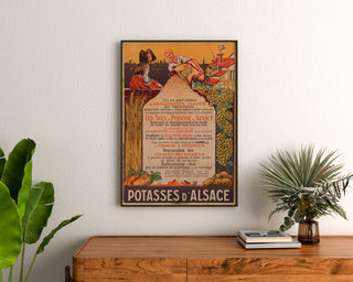 Manifesto pubblicitario vintage Potasses d’Alsace, incorniciato sopra una cassettiera in legno, tra piante.