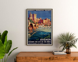 Manifesto turistico vintage – Avignone, Francia romanica e medievale, incorniciato sopra una cassettiera di legno, tra piante.
