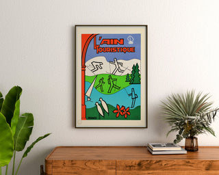 Manifesto turistico vintage – L’Ain touristique, incorniciato sopra una credenza in legno, tra piante.