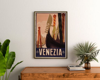 Manifesto turistico vintage – Venezia, prue di gondole, incorniciato sopra una cassettiera in legno, tra piante.