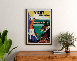 Manifesto turistico vintage – Vichy, sorgenti e turismo, incorniciato sopra una cassettiera in legno, tra piante.