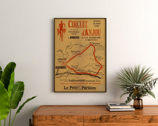 Manifesto vintage Circuit d’Anjou, marcia, incorniciato sopra un comò in legno, tra piante.