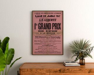 Manifesto vintage Grand Prix de Lyon, marcia, incorniciato sopra una cassettiera in legno, tra piante.