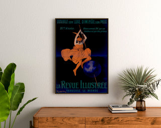 Poster vintage La Revue illustrée, incorniciato sopra una cassettiera in legno, tra piante.