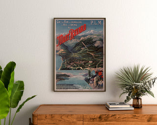 Manifesto vintage Mont-Revard, ferrovia a cremagliera, incorniciato sopra una cassettiera in legno, tra piante.