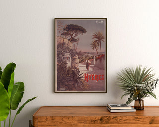 Poster vintage P. L. M. Hyères, incorniciato sopra una cassettiera in legno, tra piante.