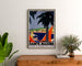 Poster vintage Sainte-Maxime, Costa dei Maures, incorniciato sopra una cassettiera in legno, tra piante.